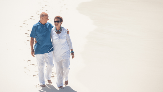 Ein älteres Paar, das arm in arm über einen strand läuft, während sie den Sonnenuntergang genießen.
